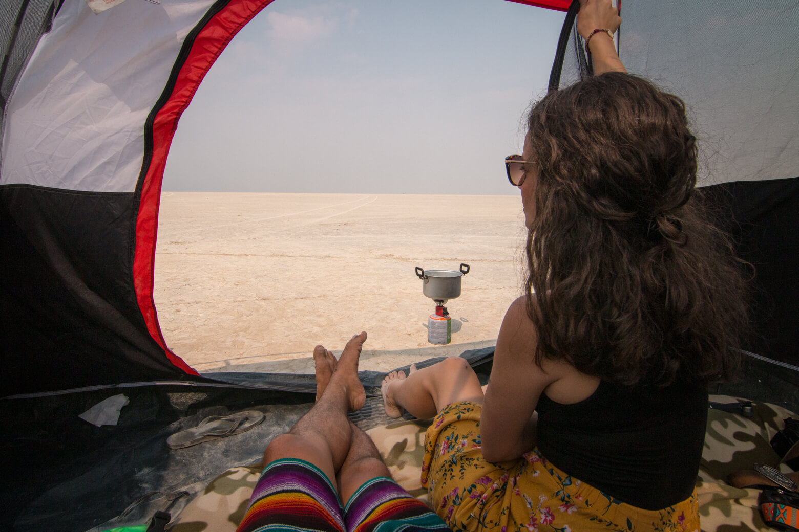 Nina and Garrett inside a small red tent looking out onto the Alvord Desert while boiling water on a jet boil.