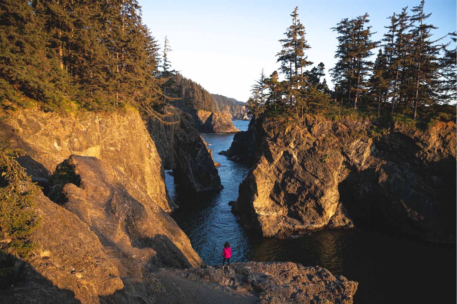 Tiny hiker in pink jacket overlooking the ocean and beautiful seastacks and rocks in the distance.