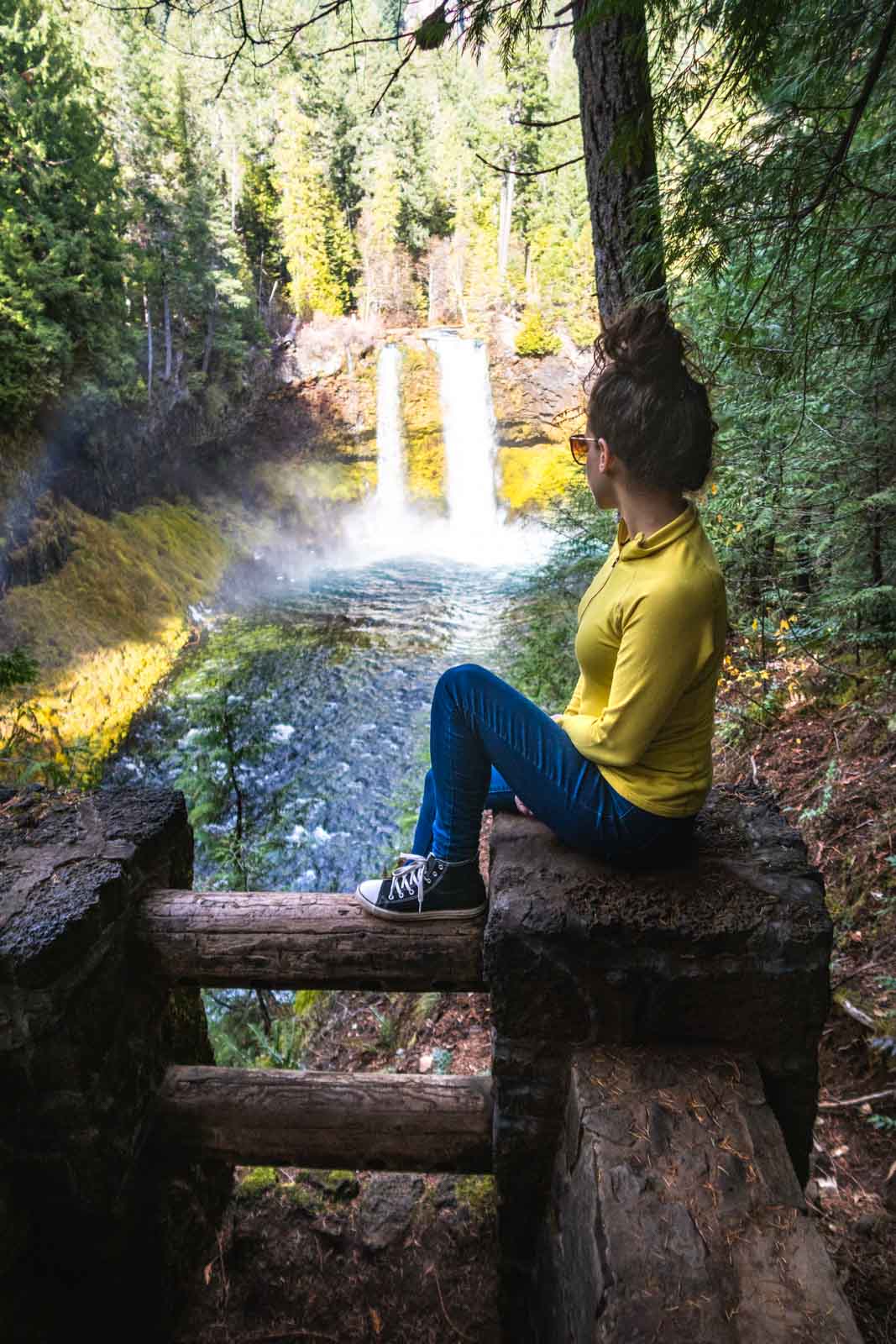 Koosah Falls with Nina sitting on a wooden fence overlooking the falls.