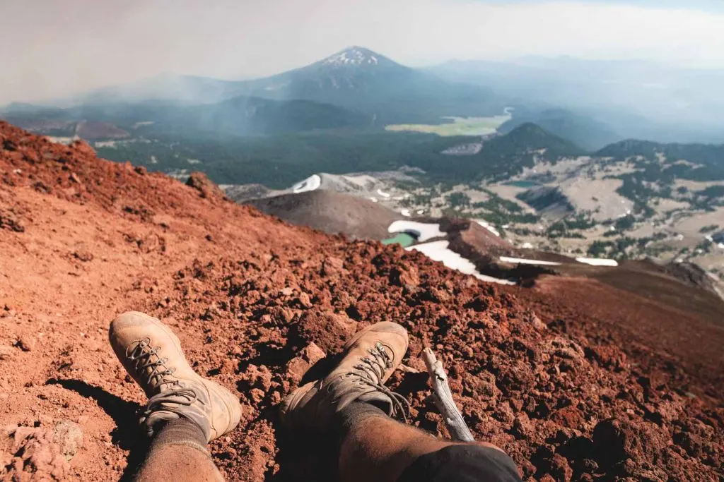Hiker's legs on mountain top with mountain and glacier views in front while hiking south sister