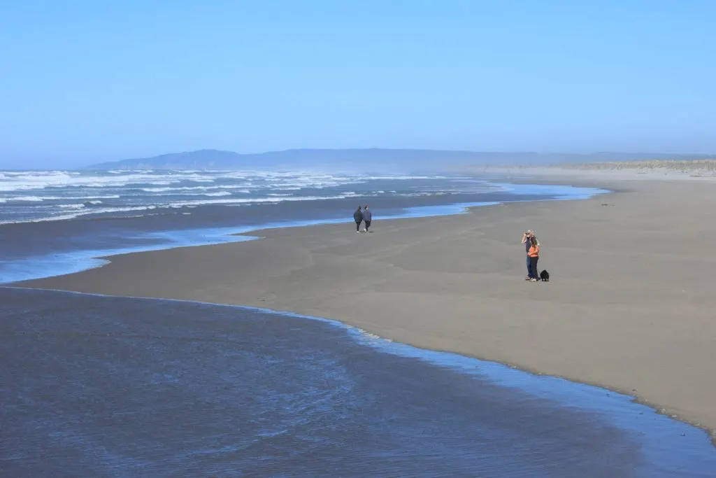 View of people walking on Bullards Beach near one of the best Oregon Lighthouses 