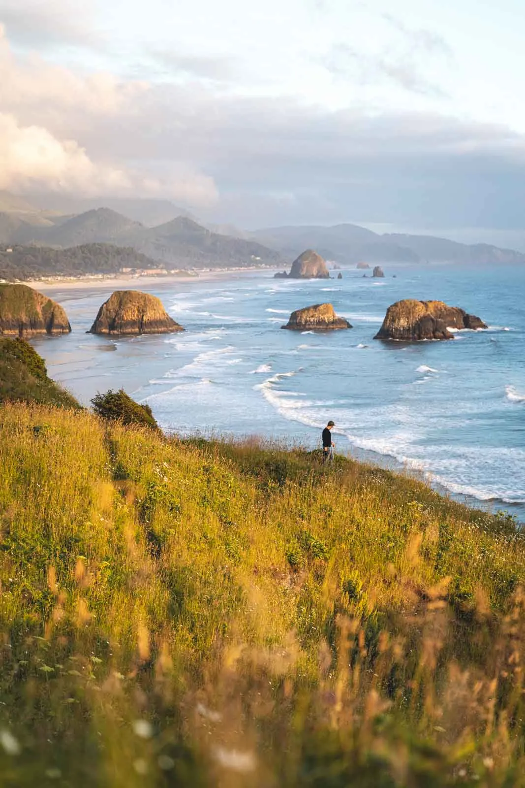 View of person on grassy cliff with the ocean and rocky islands in the background at Ecola State Park on the Oregon Coast