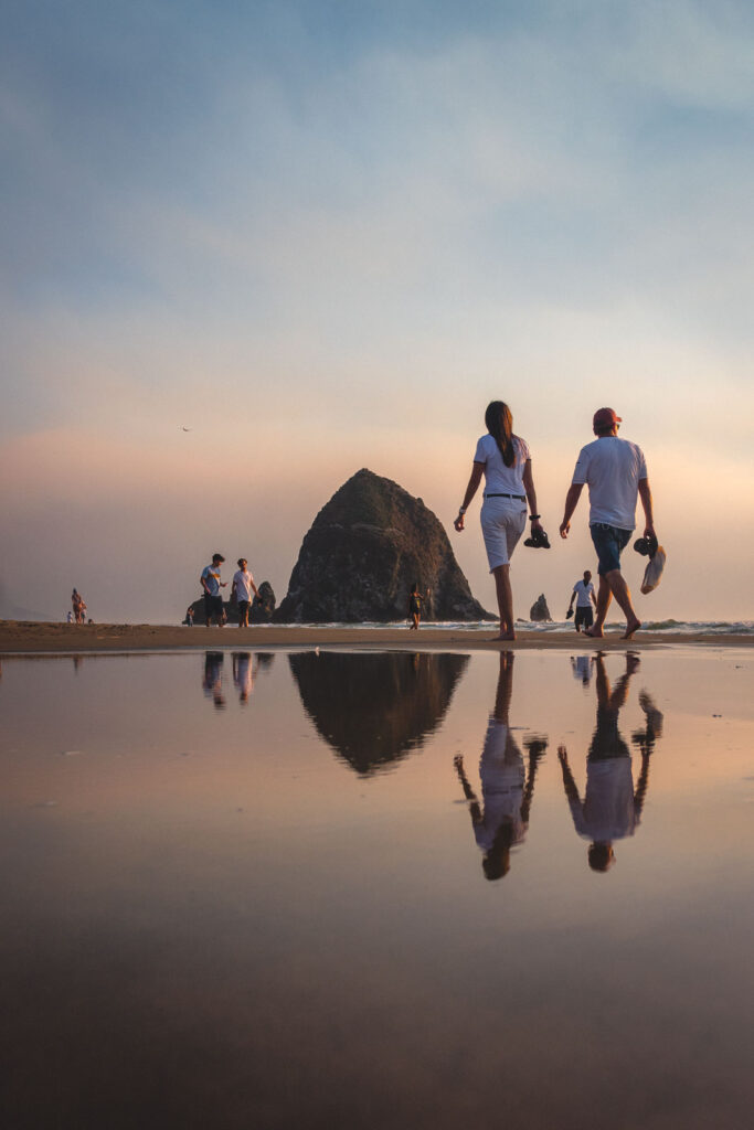 Two people walking on a Cannon Beach at sunset.