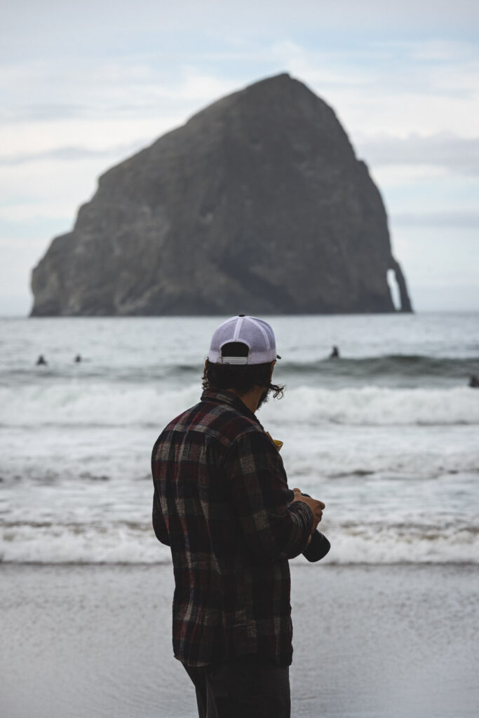 Man standing with camera and looking out to rock island in ocean at Cape Kiwanda, one of the Oregon Coast beaches