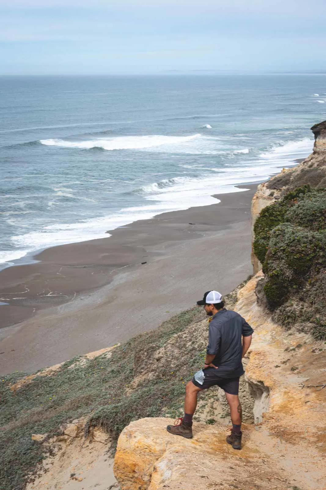 Man hiking and looking out over beach and ocean at Floras Lake State Park, home to one of the best beaches in Oregon