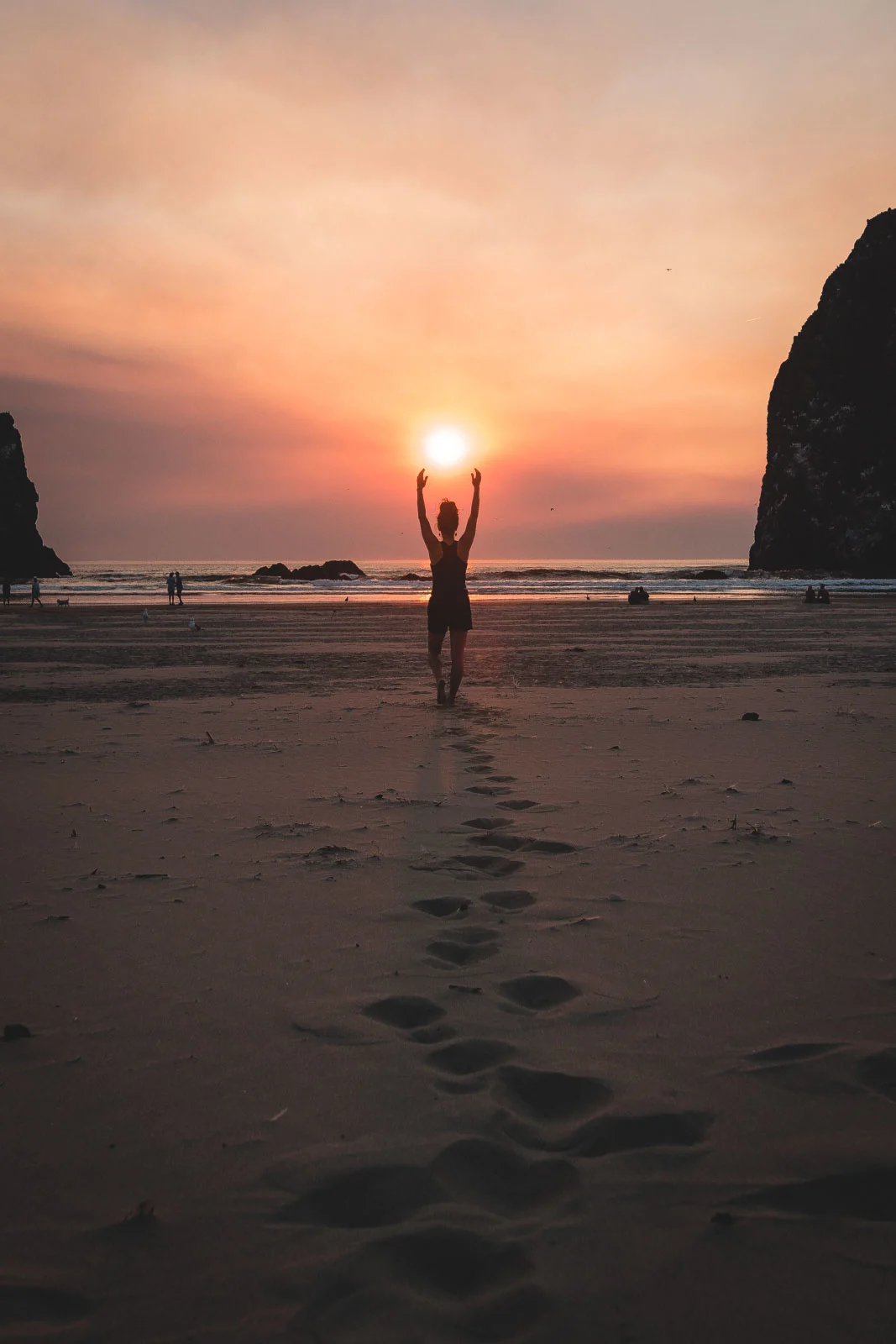 Person standing on beach with arms up to setting sun at Cannon Beach, one of the best Oregon Coast beaches