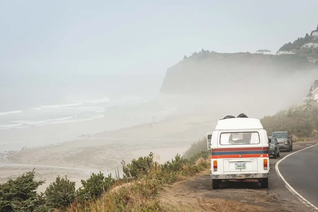 VW van on cliffside with foggy beach and seacliffs in distance at Oceanside Beach in Oregon