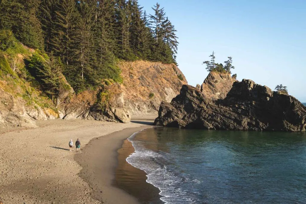 Secret Beach in Oregon with people walking on beach and sea cliffs and rocky outcrop in background