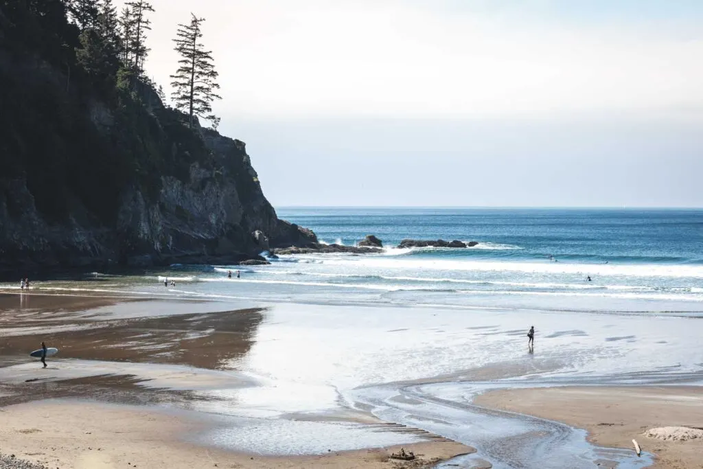 Beach at low tide with person walking on beach and rock outcrop to left of frame at Short Sands Beach in Oregon