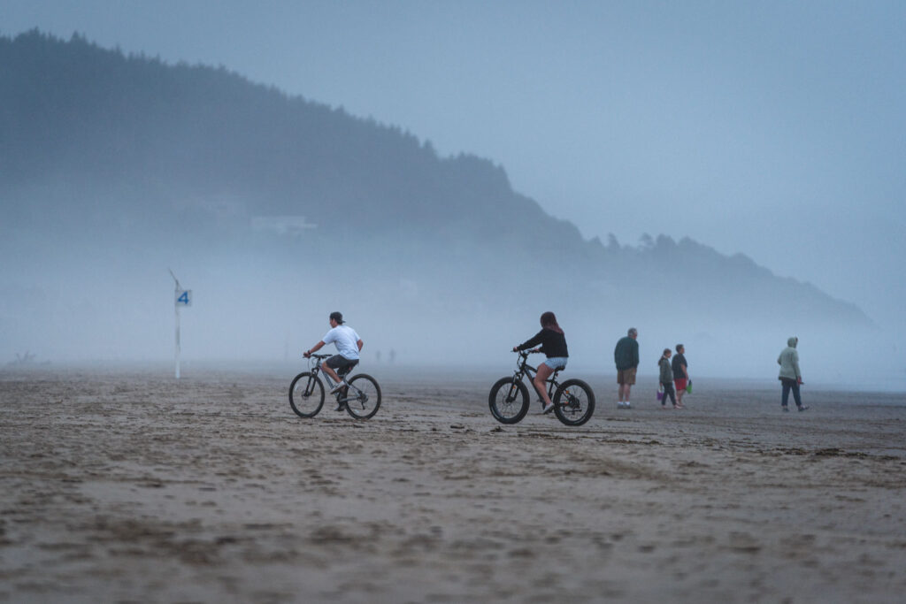 Bikers on fat bikes on a foggy beach - one of the things to do in Newport Oregon