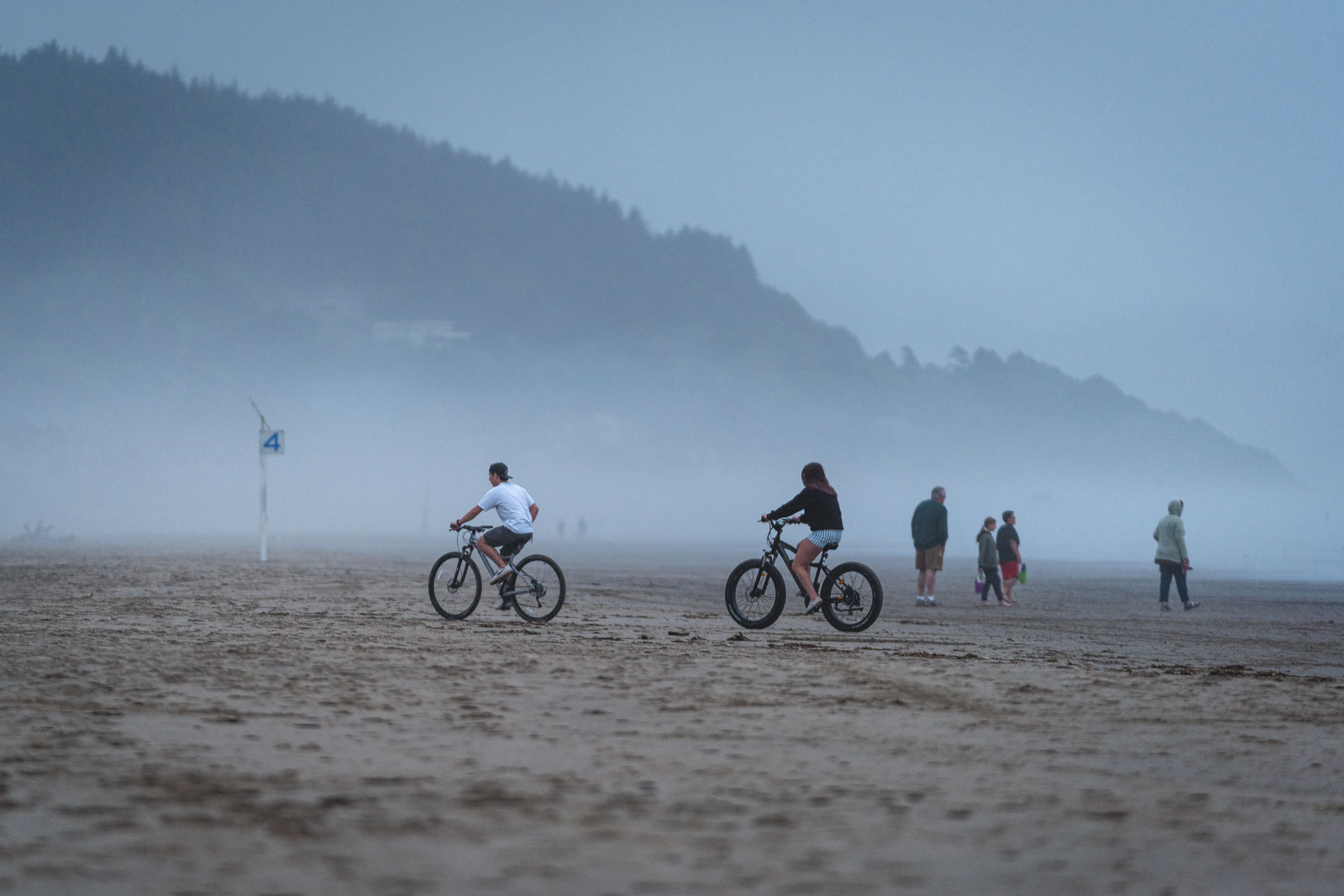 Bikers on fat bikes on a foggy Otter Rock Beach near Newport.
