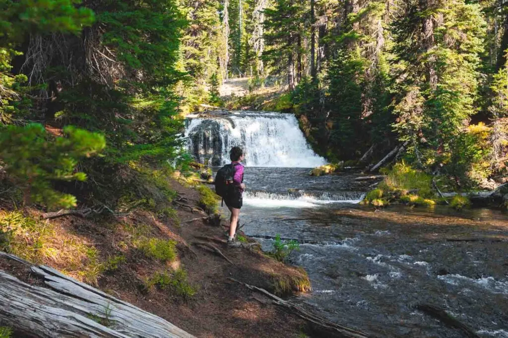 Woman standing in front of waterfall on the Green Lakes trail