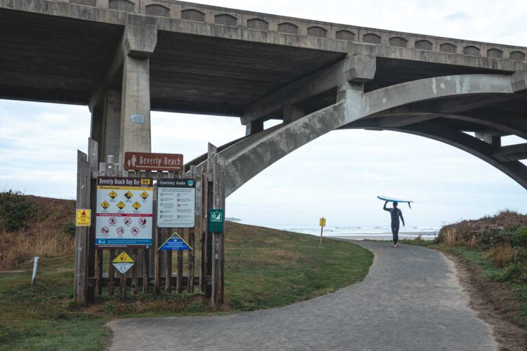 Surfer with surfboard walking to beach under bridge at Beverly Beach State Park