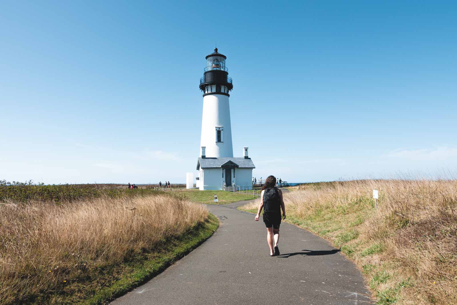 Nina walking towards Yaquina Head Lighthouse, a black and white lighthouse.