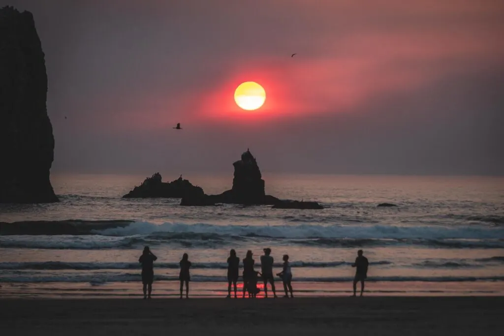 People on beach watching sunset on Cannon Beach out to ocean and rocky island