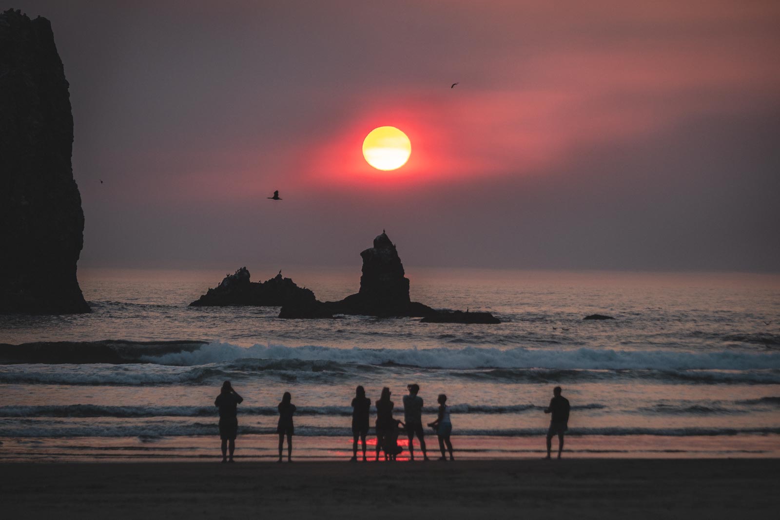 People on beach watching sunset on Cannon Beach out to ocean and rocky island.