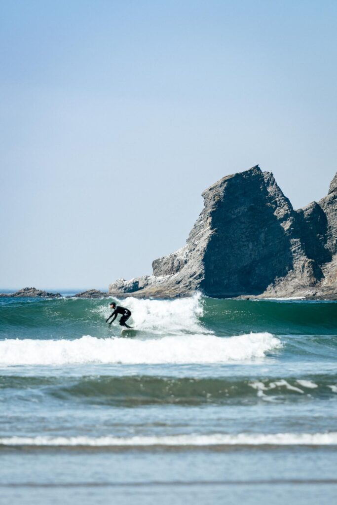 Surfer surfing a wave with rocky outcrop in background at Short Sand Beach near Cannon Beach