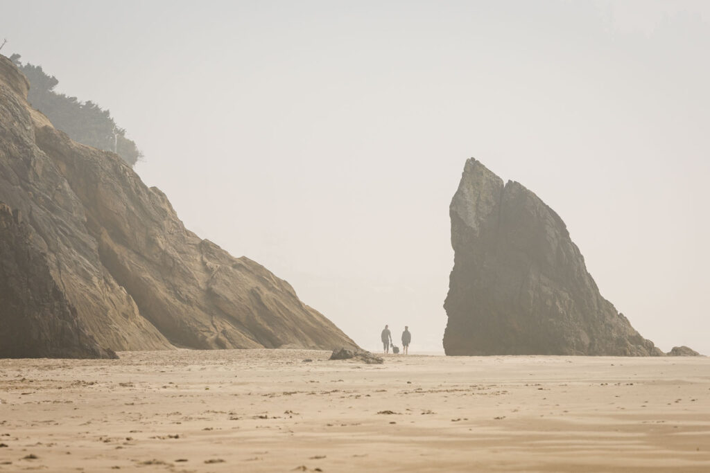 Misty view of people walking on a beach in the distance surrounded by large rocks at Hug Point