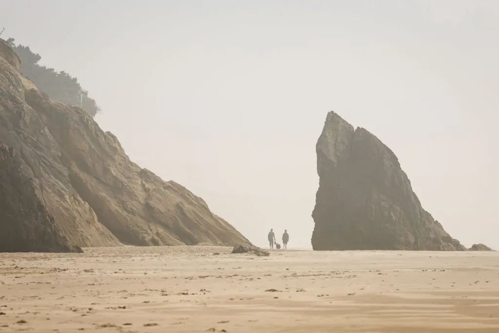 Misty view of people walking on a beach in the distance surrounded by large rocks at Hug Point