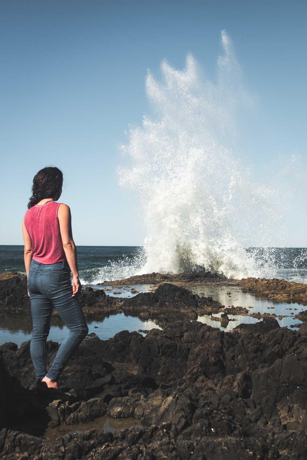Woman standing and looking out over ocean blowhole at Devil's Churn in Oregon