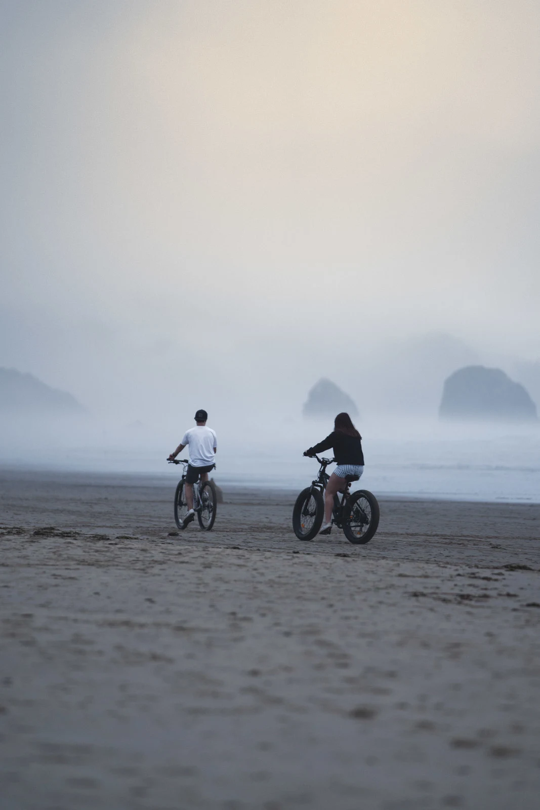 Two people fat biking on a foggy beach in Lincoln City