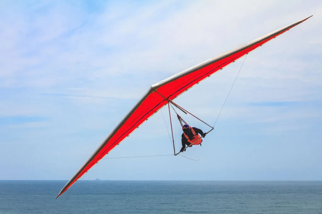 Hang gliding man flying on an orange wing near Pacific City, Oregon