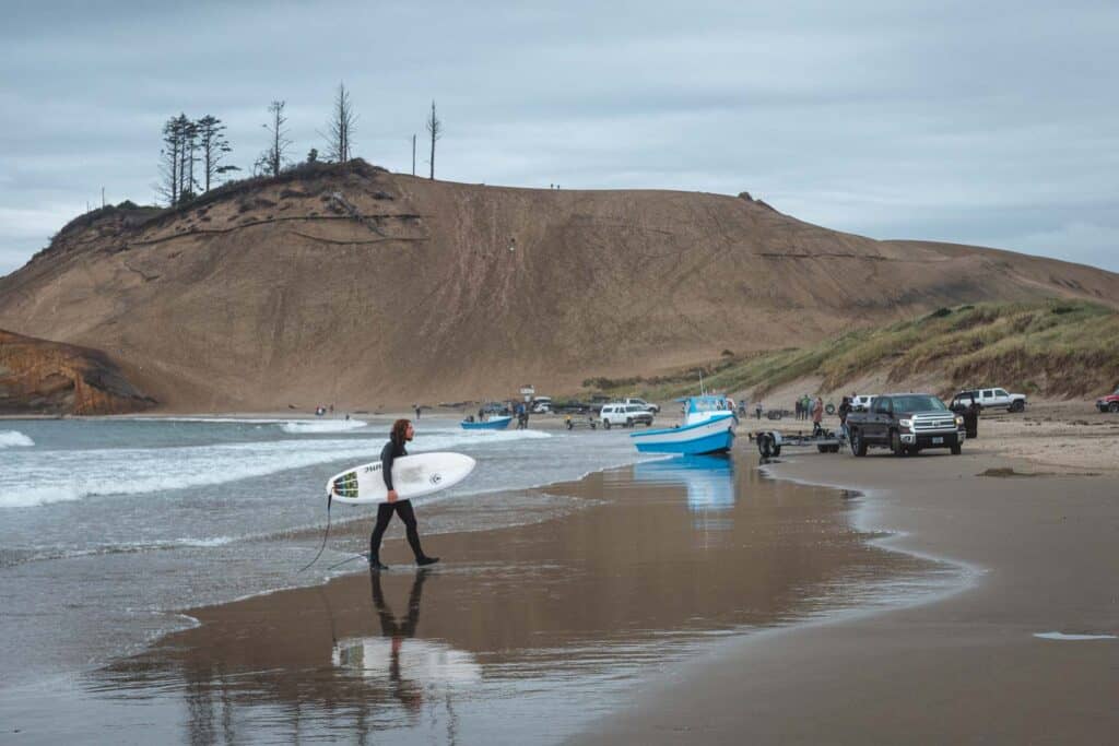 Surfer with surfboard walking out of the ocean with giant sand dune in background at Cape Kiwanda