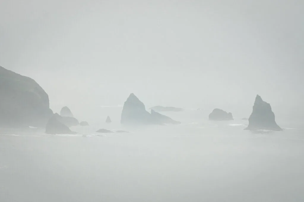 Large rocks sticking out of the sand on a foggy beach at Three Arch Rock Wilderness near Cape Meares