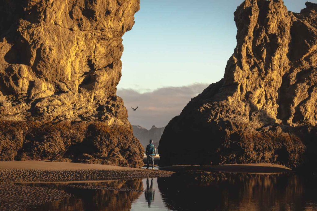 Person walking amongst sea cliffs at Bandon Beach.