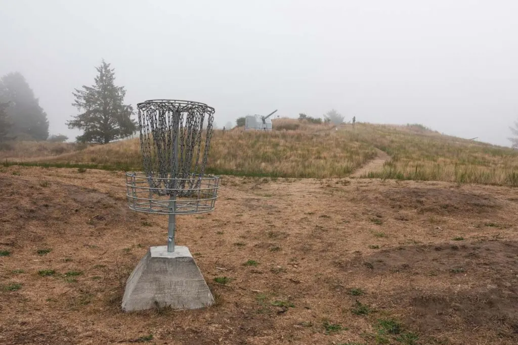 Disk golf basket on scrubby hill in Fort Stevens State Park