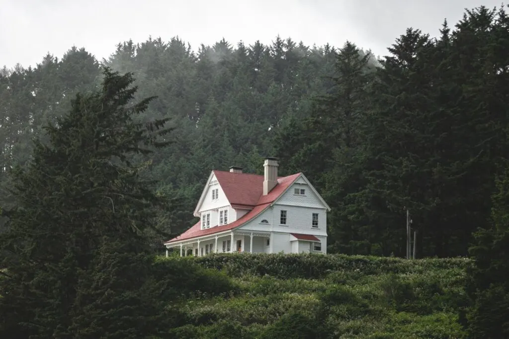 White house with red roof on a hill with forest in background at Heceta Head