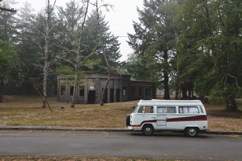 VW bus parked in front of ruins in the trees at Fort Stevens State Park