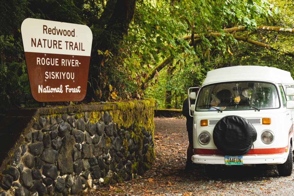 VW van parked beside stone wall with Redwoods Nature Trail side on top and surrounded by woods