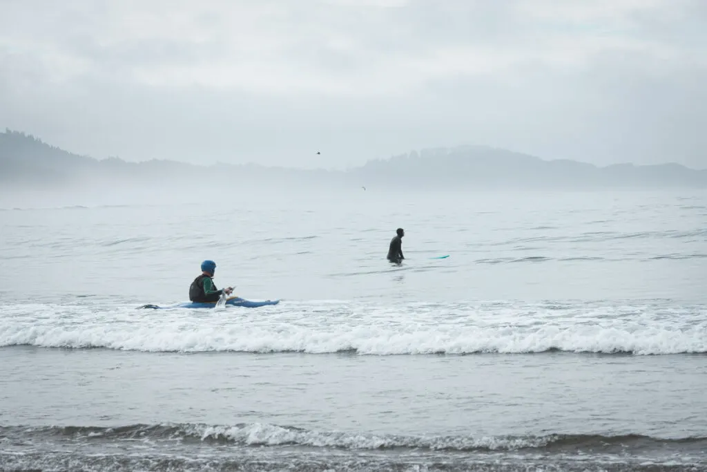 Two surfers in the ocean at Devils Punch Bowl beach in Oregon
