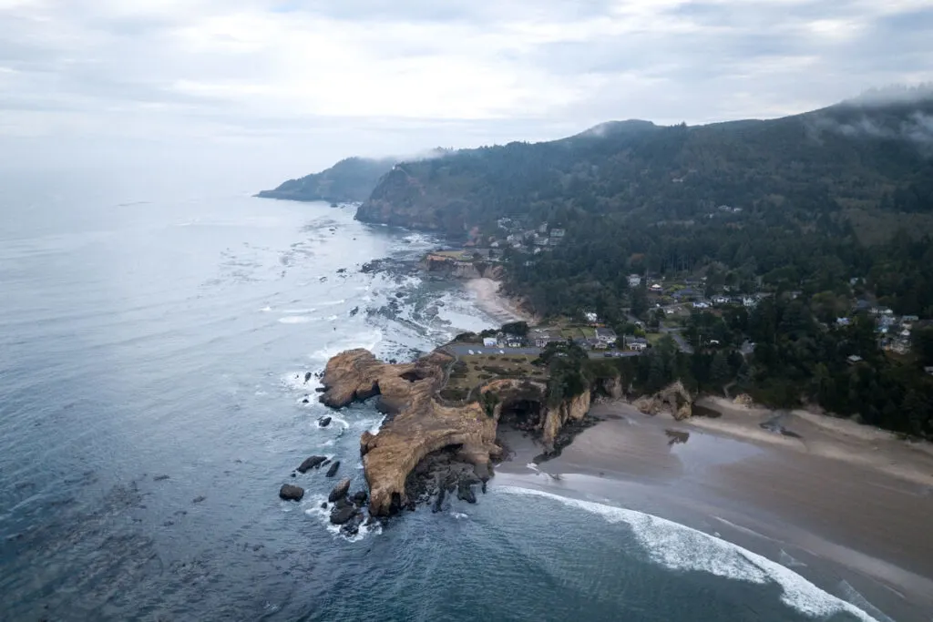 Aerial view over rocky outcrop and Devils Punch Bowl with beach on each side and forest behind it