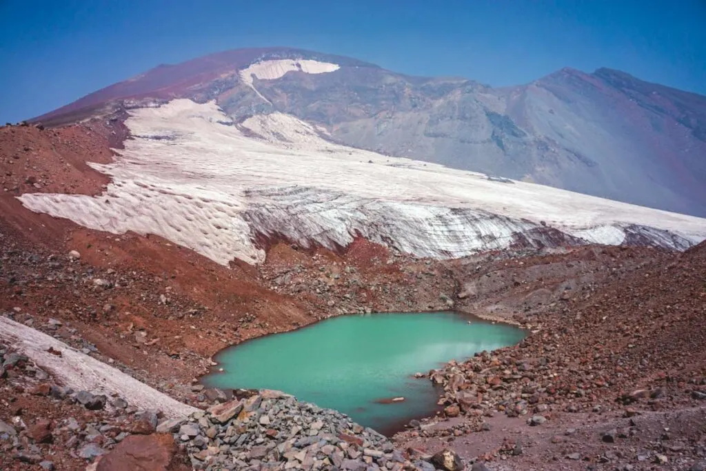 Turquoise lake surrounded by mountains with snow while hiking south sister