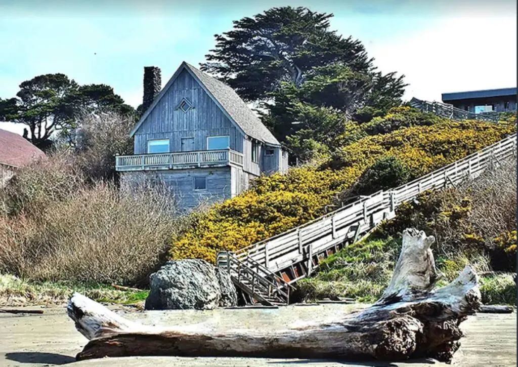 Old rustic beach cabin in oregon overlooking the beach with a large driftwood log in foreground