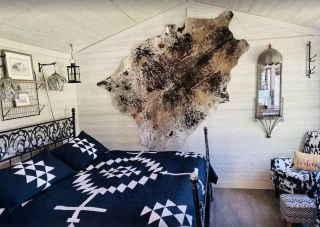 Inside of Cow Camp cabin in Oregon with king size bed with blue and white coverlet, animal skin hanging on wall