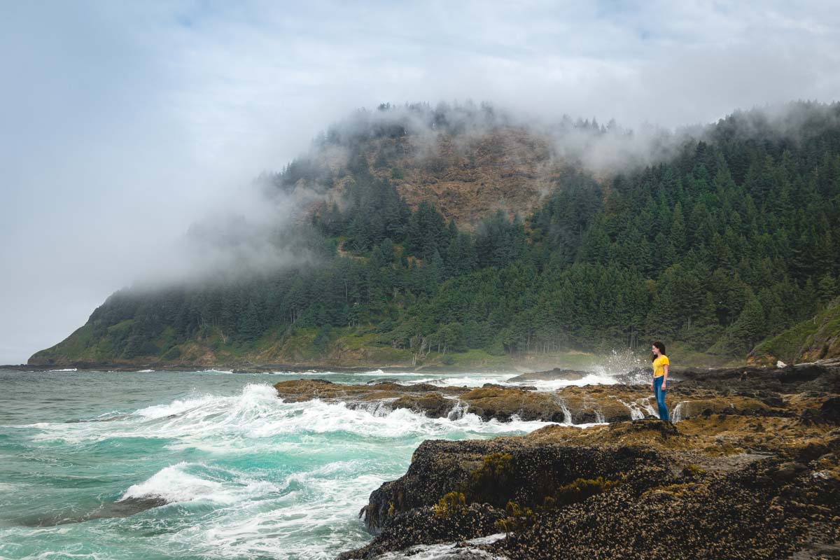 Nina at Cape Perpetua on a rocky cliffside edge with the ocean roaring on the left.