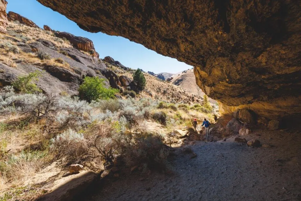 Hikers enter a small cliffside cave on the Juniper Gulch.