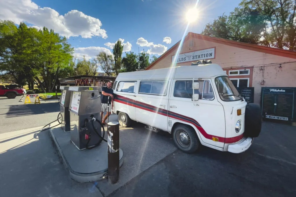 A man filling up a white campervan with gas at Fields gas station in Oregon.
