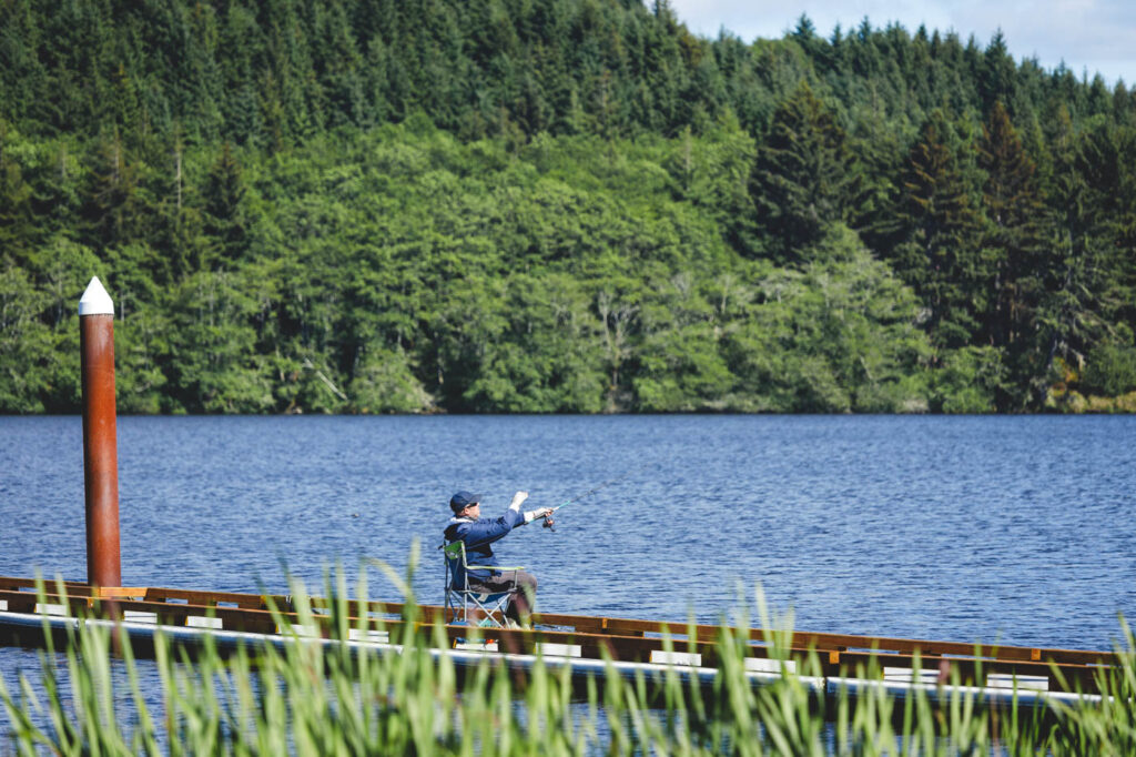 A fishermen at Cullaby Lake Country Park surrounded by forest casting his rod.