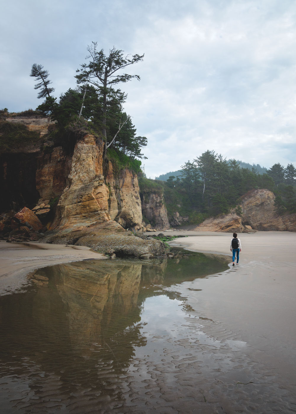 Nina walking along a beach beside a cliff in Devil's Punchbowl State Park in Oregon.