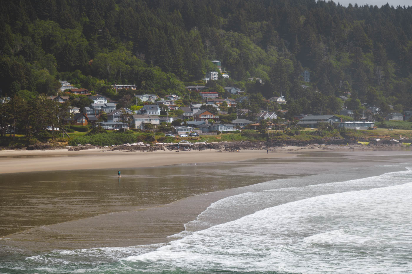 A few tourists walking along Yachats Beach with houses and trees in the background in Oregon.