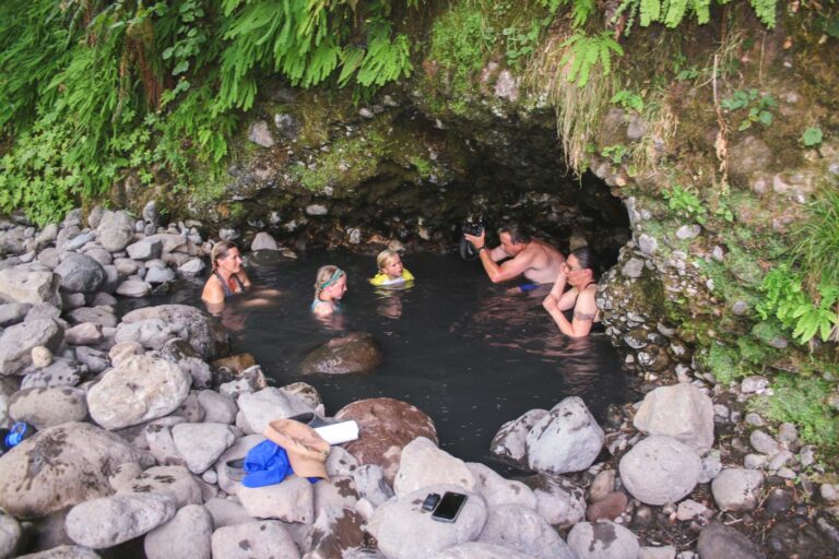A dad taking photos of his family while bathing inside Bigelow Hot Springs surrounded by rocks and grass.