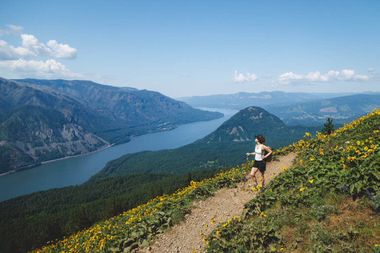 Nina hiking along a trail on Dog Mountain with a crazy view over Columbia River Gorge on a sunny day.