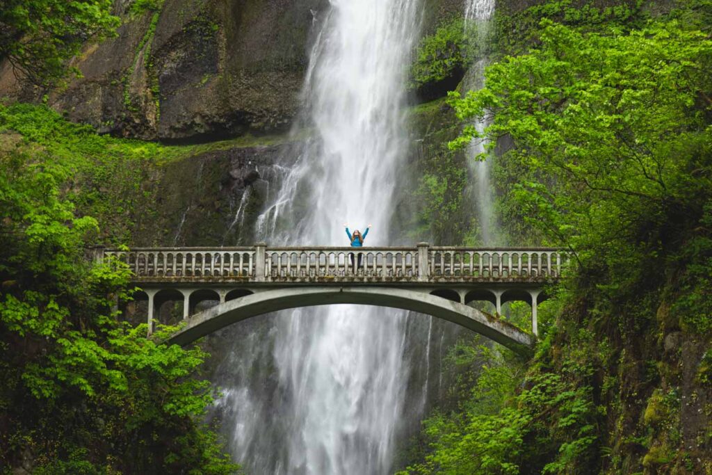 Nina celebrating with her hands up while on a bridge at Multnomah Falls.