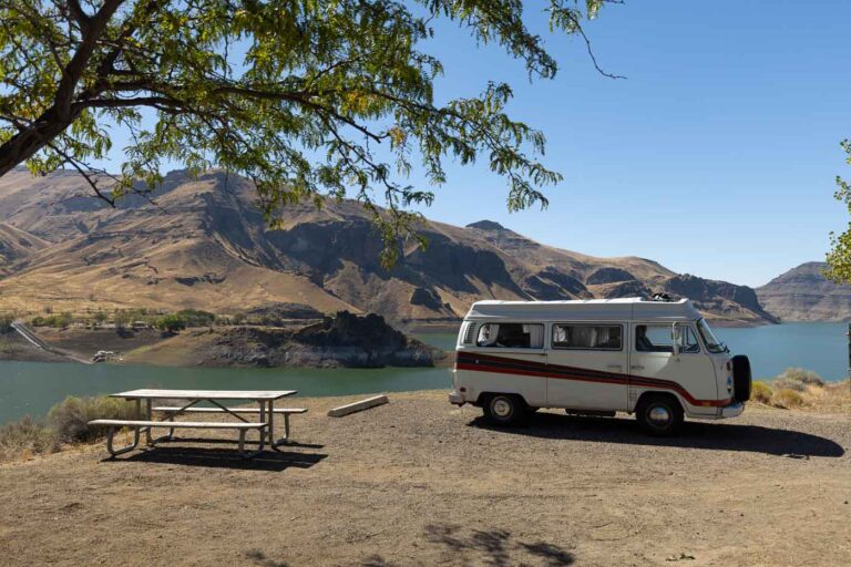 VW Bus parked at Lake Owyhee State park campground with cliffs in the back as well as the lake below.