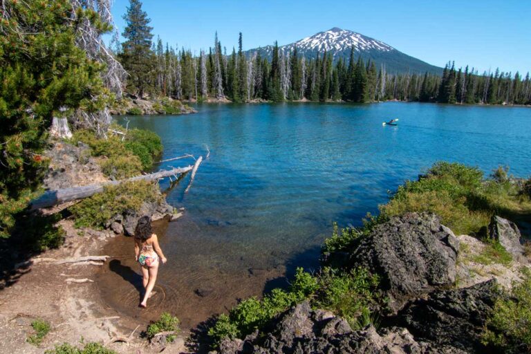 Nina walking into a lake with a kayaker and a mountain in the distance.