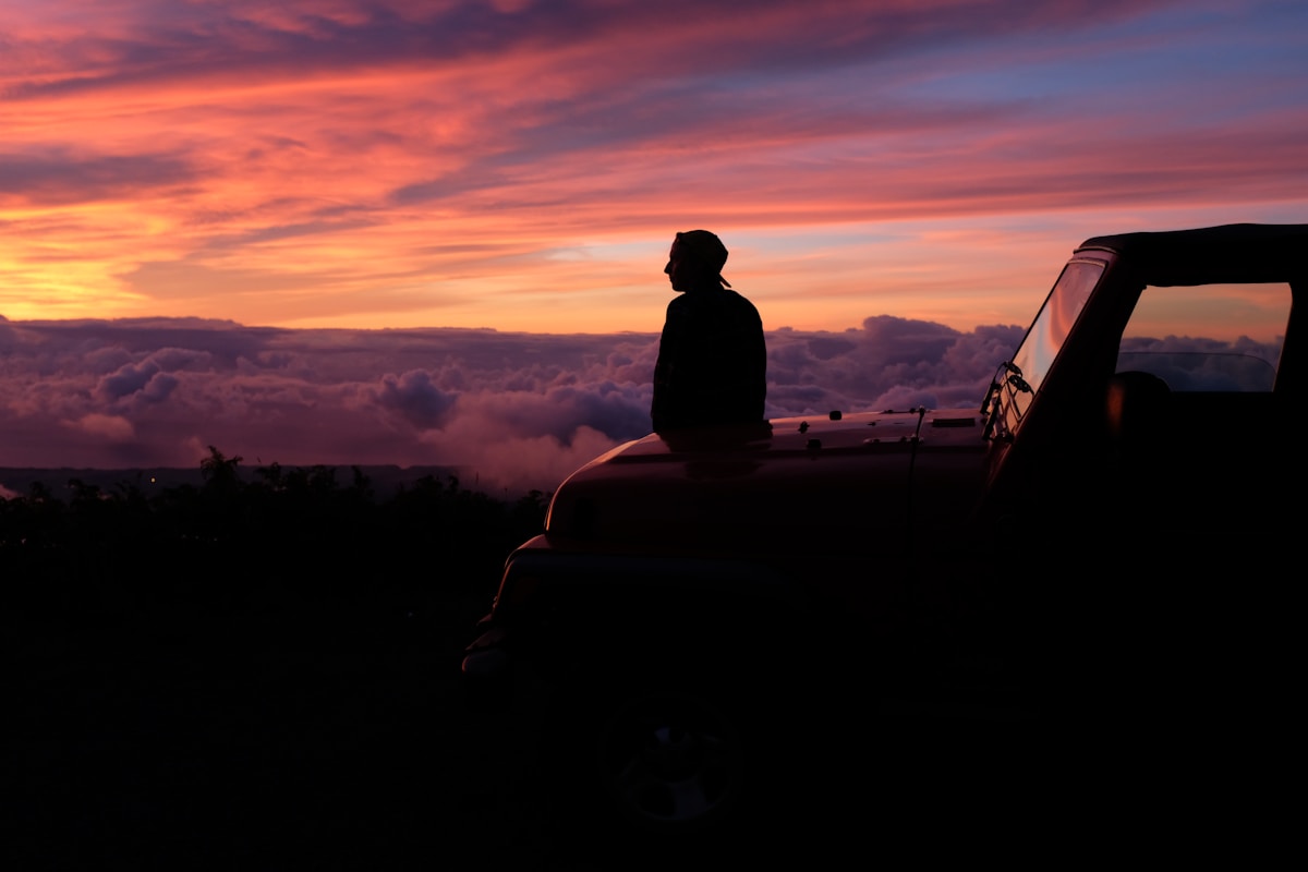 man sitting on car hood watching the skies under golden hour